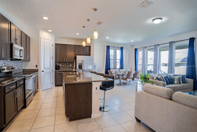 kitchen featuring a kitchen bar, a kitchen island with sink, stainless steel appliances, and tasteful backsplash