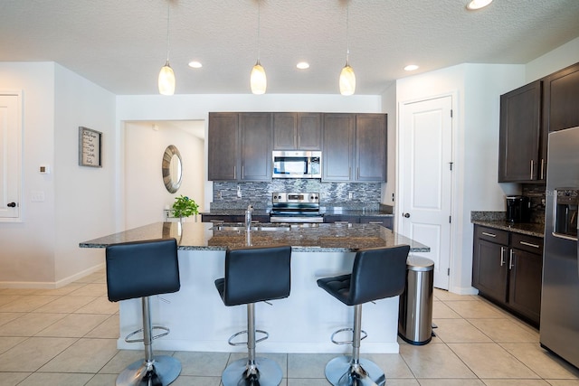 kitchen featuring pendant lighting, a center island with sink, appliances with stainless steel finishes, and a textured ceiling