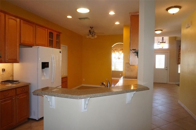 kitchen featuring tasteful backsplash, a kitchen breakfast bar, kitchen peninsula, a healthy amount of sunlight, and white refrigerator with ice dispenser