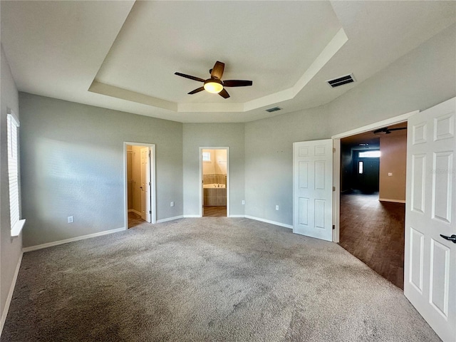 unfurnished bedroom featuring ceiling fan, a raised ceiling, ensuite bathroom, and carpet floors