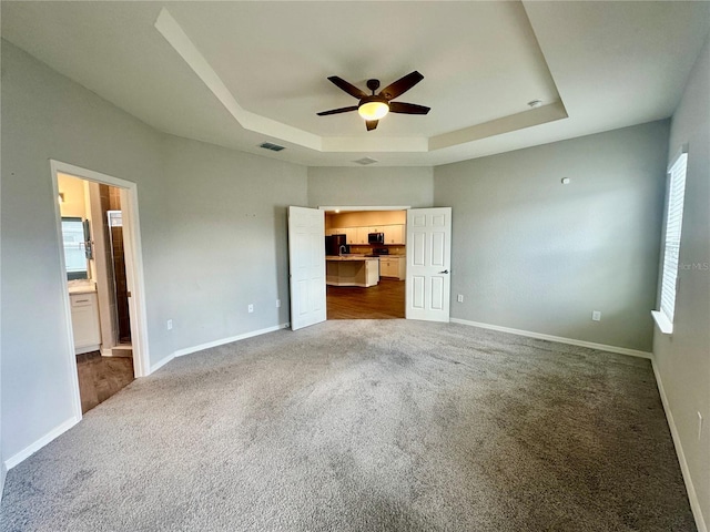 unfurnished bedroom featuring carpet flooring, a tray ceiling, ensuite bath, and ceiling fan