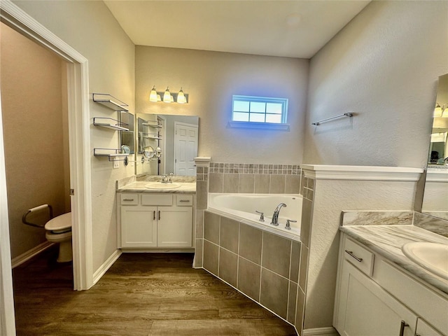 bathroom featuring a relaxing tiled tub, hardwood / wood-style flooring, vanity, and toilet