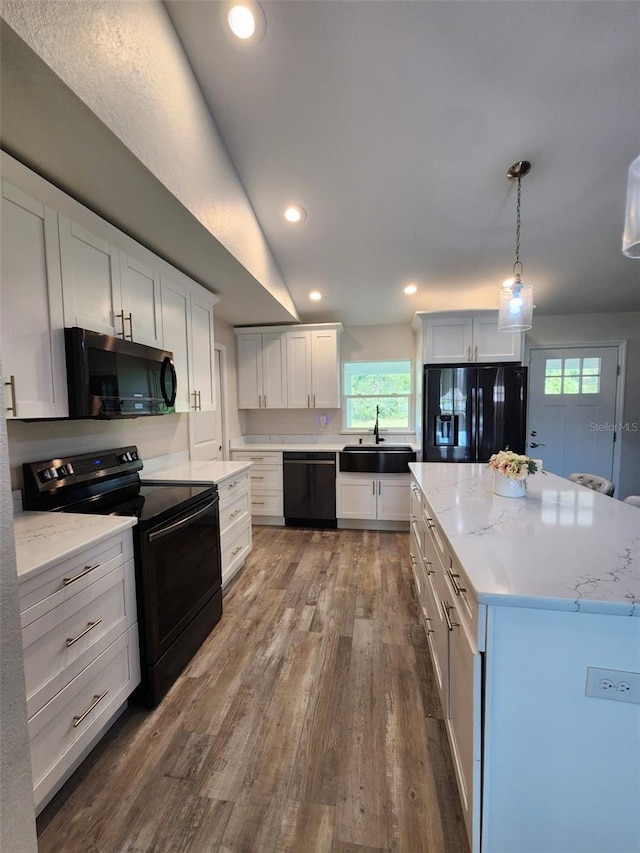 kitchen with hardwood / wood-style floors, hanging light fixtures, white cabinetry, black appliances, and sink