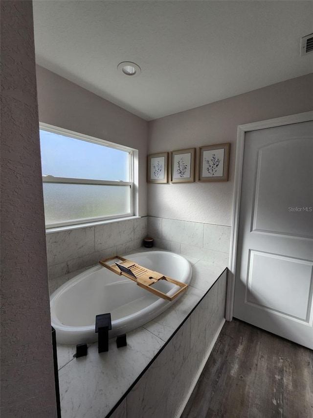 bathroom with wood-type flooring and tiled bath