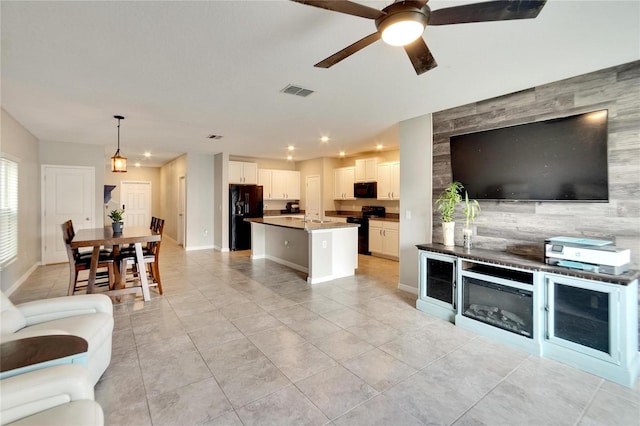 kitchen featuring an island with sink, white cabinets, black appliances, decorative light fixtures, and ceiling fan