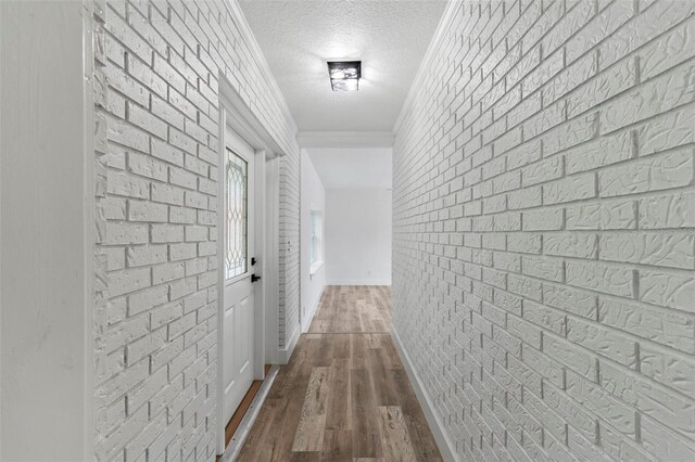 corridor with brick wall, hardwood / wood-style flooring, ornamental molding, and a textured ceiling