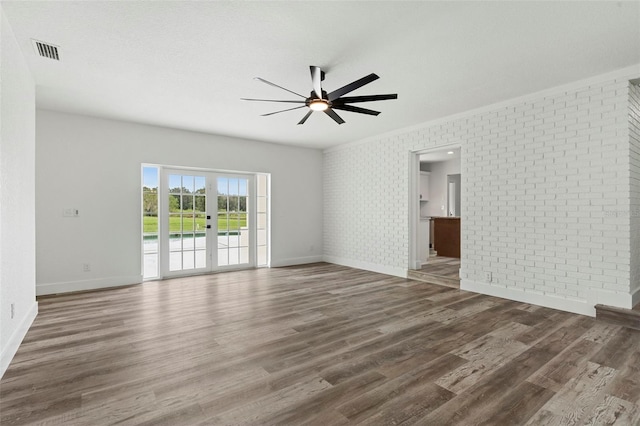 unfurnished living room with visible vents, wood finished floors, brick wall, baseboards, and ceiling fan