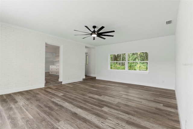 interior space featuring wood finished floors, ceiling fan, brick wall, and visible vents