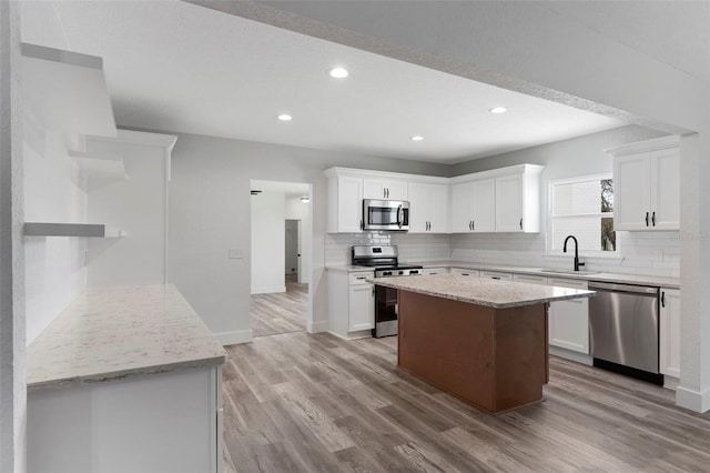 kitchen with white cabinets, sink, appliances with stainless steel finishes, light stone countertops, and light hardwood / wood-style floors