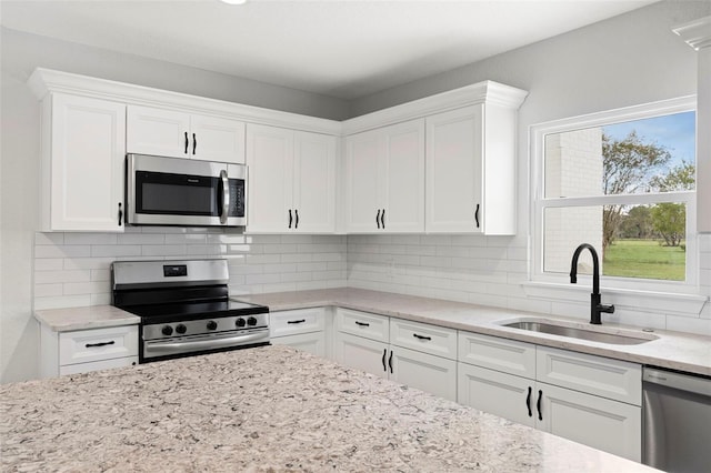 kitchen featuring tasteful backsplash, sink, white cabinets, stainless steel appliances, and light stone countertops