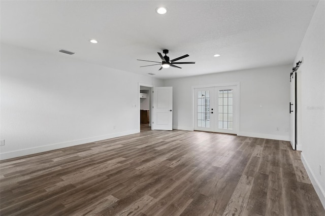 empty room with ceiling fan, french doors, a textured ceiling, dark wood-type flooring, and a barn door