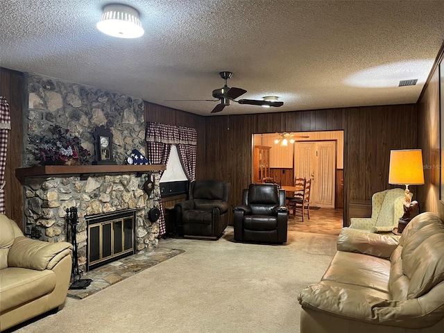 living room with a stone fireplace, wood walls, a textured ceiling, ceiling fan, and light carpet