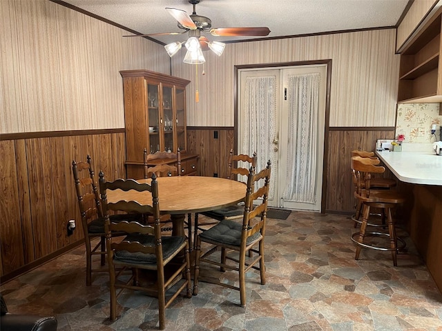 dining space featuring a textured ceiling, crown molding, wood walls, and ceiling fan