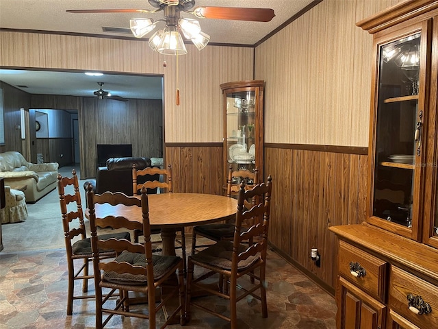 dining space featuring ornamental molding, wooden walls, a textured ceiling, and ceiling fan