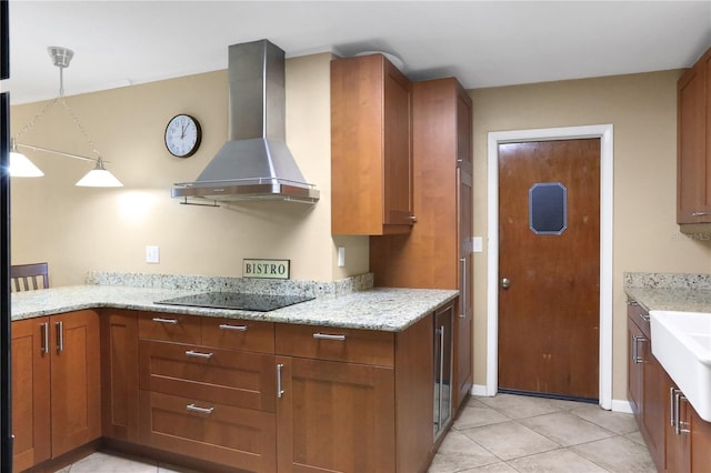 kitchen with pendant lighting, black electric stovetop, light stone counters, wall chimney range hood, and light tile patterned floors