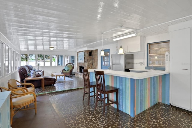 kitchen with white cabinets, stainless steel refrigerator, a fireplace, pendant lighting, and sink