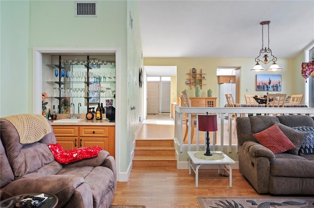 living room with an inviting chandelier, sink, and light hardwood / wood-style floors