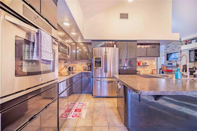 kitchen featuring stainless steel appliances, light tile patterned flooring, vaulted ceiling, a kitchen breakfast bar, and backsplash