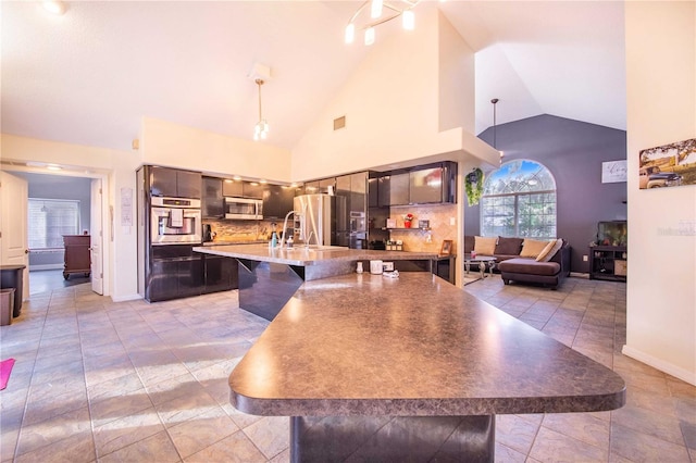 kitchen featuring a breakfast bar area, sink, stainless steel appliances, backsplash, and high vaulted ceiling