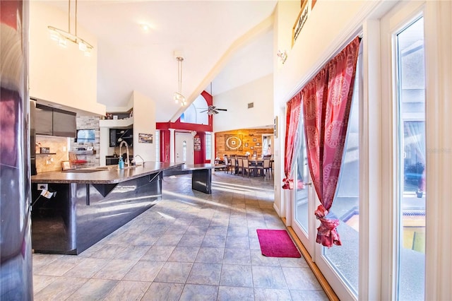 kitchen with high vaulted ceiling, ceiling fan, decorative backsplash, hanging light fixtures, and a breakfast bar area