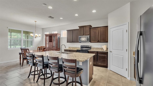 kitchen with appliances with stainless steel finishes, sink, hanging light fixtures, a breakfast bar area, and an island with sink