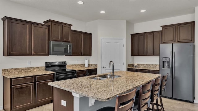 kitchen with sink, stainless steel appliances, light stone counters, an island with sink, and a breakfast bar