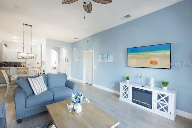 living room featuring light wood-type flooring and ceiling fan with notable chandelier