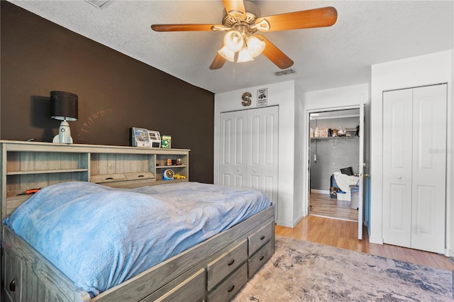 bedroom with ceiling fan, two closets, a textured ceiling, and light hardwood / wood-style flooring