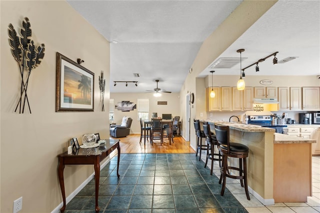 kitchen featuring ceiling fan, a breakfast bar, light brown cabinets, decorative light fixtures, and stainless steel range with electric stovetop