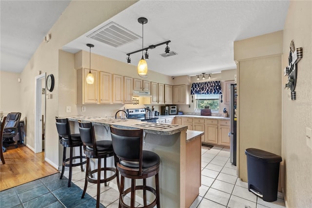 kitchen with track lighting, kitchen peninsula, appliances with stainless steel finishes, light brown cabinetry, and a kitchen bar