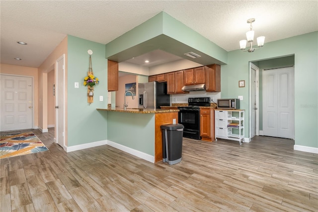 kitchen featuring light hardwood / wood-style flooring, kitchen peninsula, decorative light fixtures, appliances with stainless steel finishes, and a textured ceiling