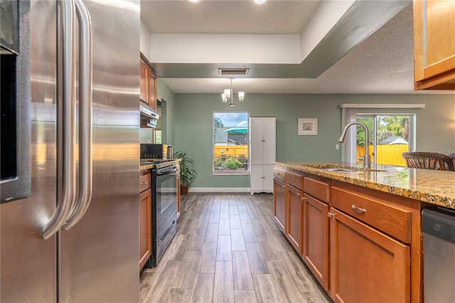 kitchen featuring hanging light fixtures, sink, appliances with stainless steel finishes, light stone counters, and light hardwood / wood-style floors