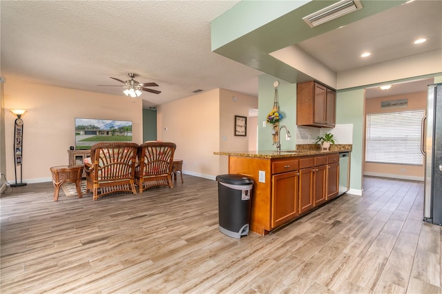 kitchen with light stone countertops, a textured ceiling, ceiling fan, stainless steel appliances, and light hardwood / wood-style flooring