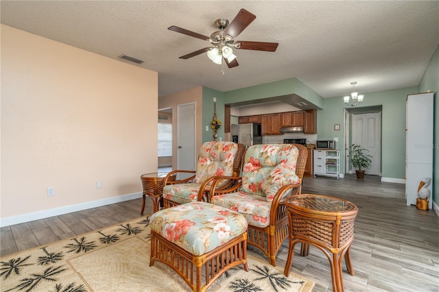 living room with ceiling fan with notable chandelier, a textured ceiling, and light hardwood / wood-style floors