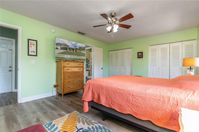 bedroom with two closets, ceiling fan, a textured ceiling, and dark hardwood / wood-style flooring