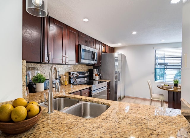 kitchen with tasteful backsplash, light stone counters, appliances with stainless steel finishes, light hardwood / wood-style flooring, and sink