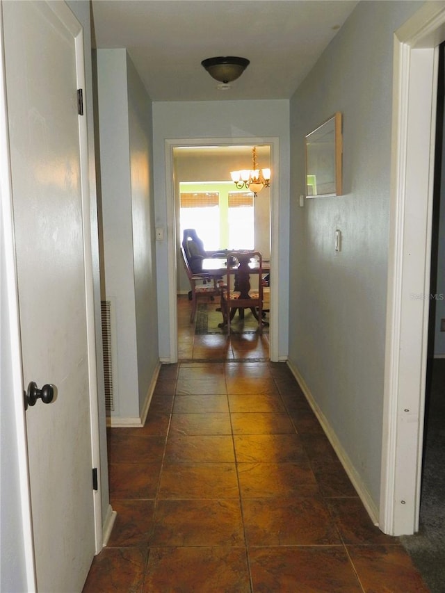 corridor with dark tile patterned flooring and an inviting chandelier