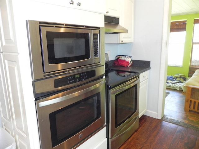 kitchen featuring white cabinetry, dark countertops, under cabinet range hood, dark wood-type flooring, and appliances with stainless steel finishes