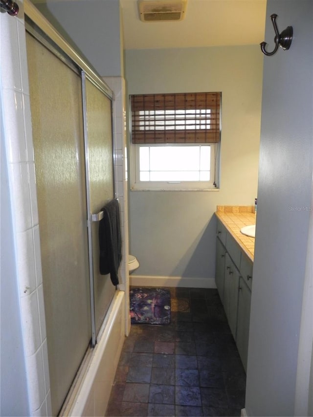 bathroom with visible vents, baseboards, combined bath / shower with glass door, vanity, and stone tile floors