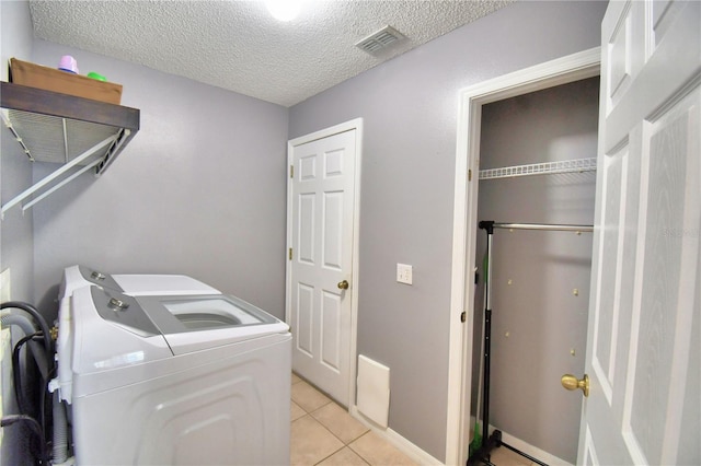 laundry room featuring a textured ceiling, light tile patterned flooring, and washing machine and clothes dryer