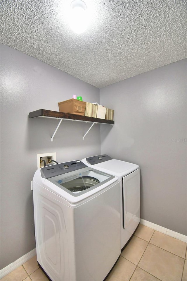 laundry room with a textured ceiling, washing machine and clothes dryer, and light tile patterned floors