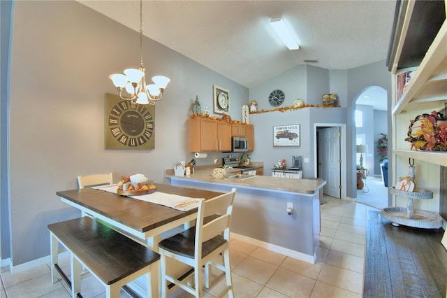 kitchen with stainless steel appliances, light tile patterned floors, kitchen peninsula, and decorative light fixtures