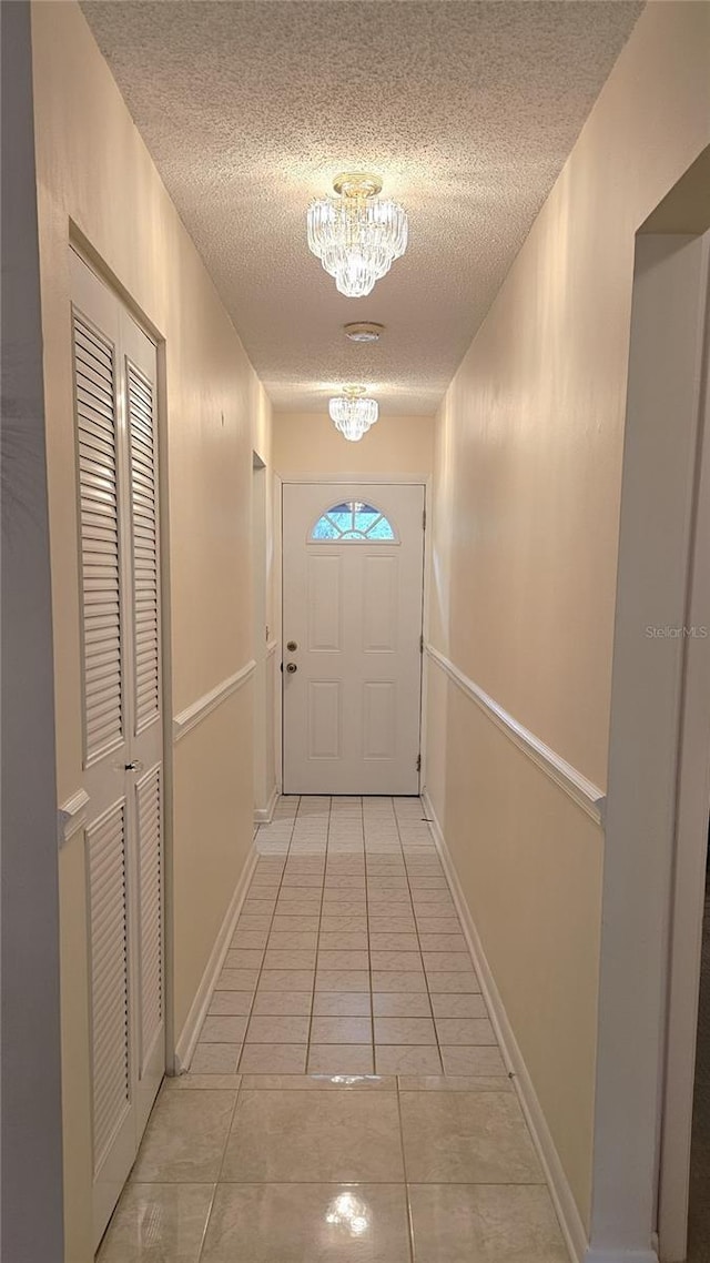 doorway to outside with light tile patterned floors, a textured ceiling, and an inviting chandelier