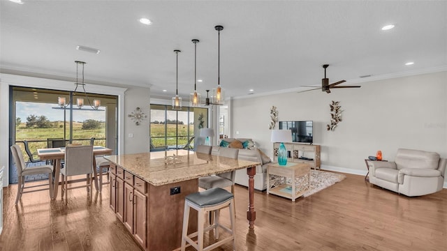 kitchen featuring ornamental molding, light stone countertops, hanging light fixtures, light hardwood / wood-style flooring, and a kitchen island