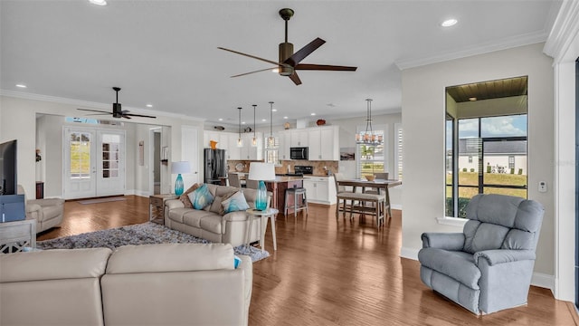 living room featuring hardwood / wood-style flooring, ceiling fan with notable chandelier, and crown molding