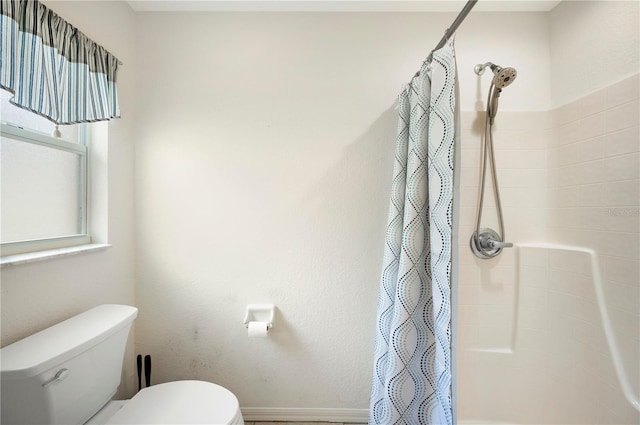 bathroom with toilet, a shower with shower curtain, and baseboards