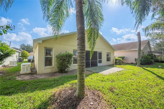 rear view of property featuring a yard, central AC unit, a patio, and stucco siding