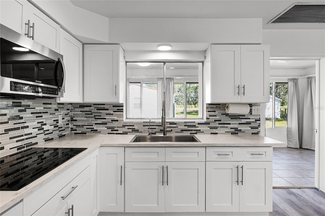 kitchen with sink, black electric cooktop, white cabinetry, light hardwood / wood-style floors, and decorative backsplash