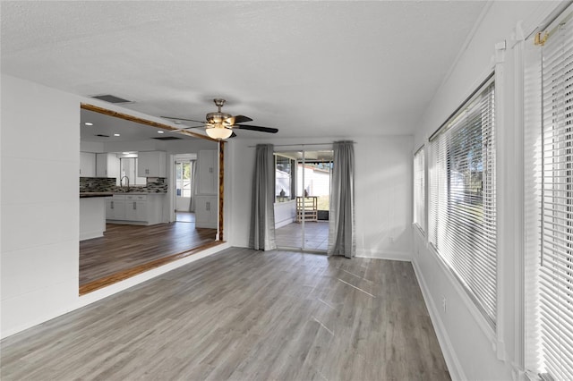 unfurnished living room featuring sink, light hardwood / wood-style flooring, a textured ceiling, and ceiling fan