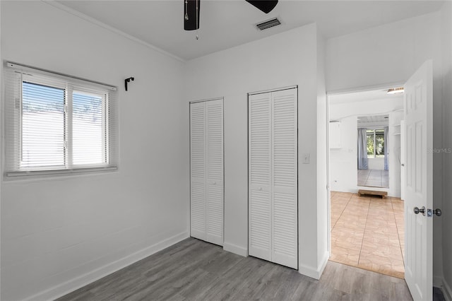 unfurnished bedroom featuring multiple closets, hardwood / wood-style flooring, and ceiling fan